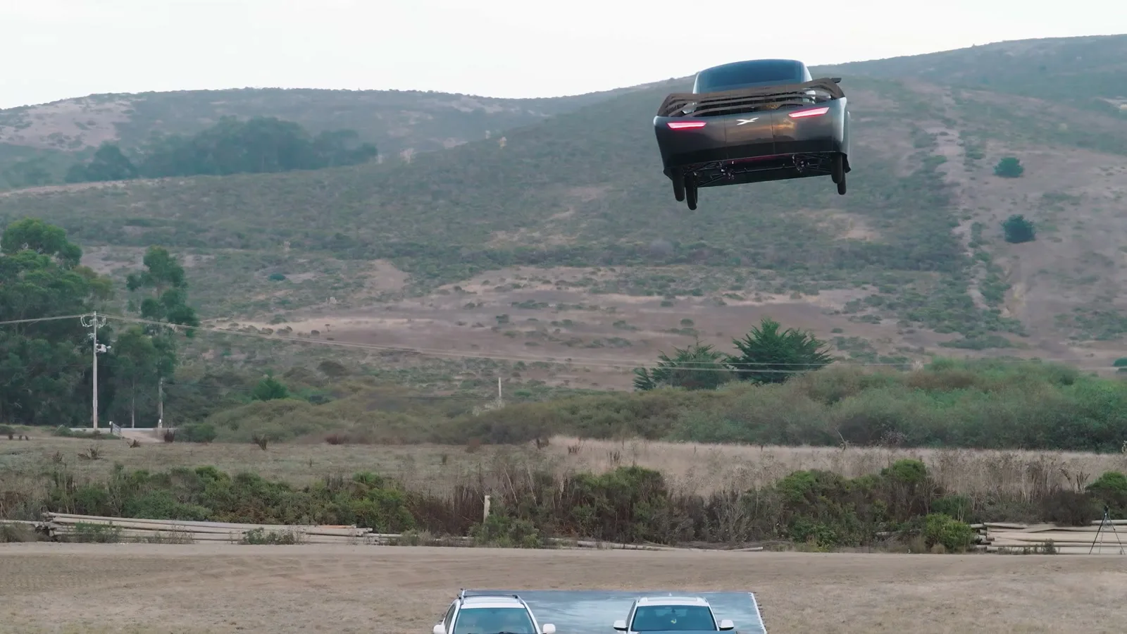 Carro voador da Alef no ar, alto sobre o campo, com morros ao fundo