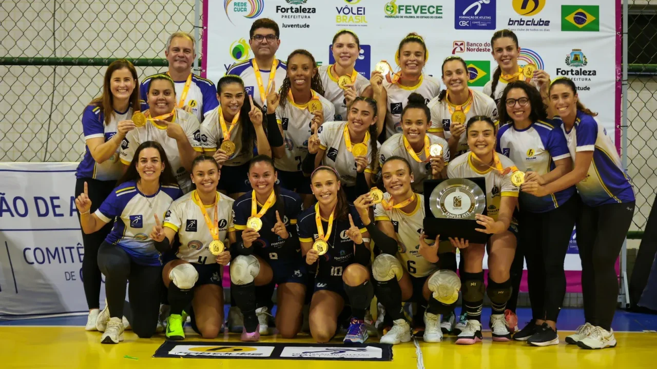 Jogadoras e comissão técnica do BNB Rede Cuca Vôlei posam com medalhas de ouro e o troféu de campeão da Superliga C feminina, em quadra na fase final em Fortaleza