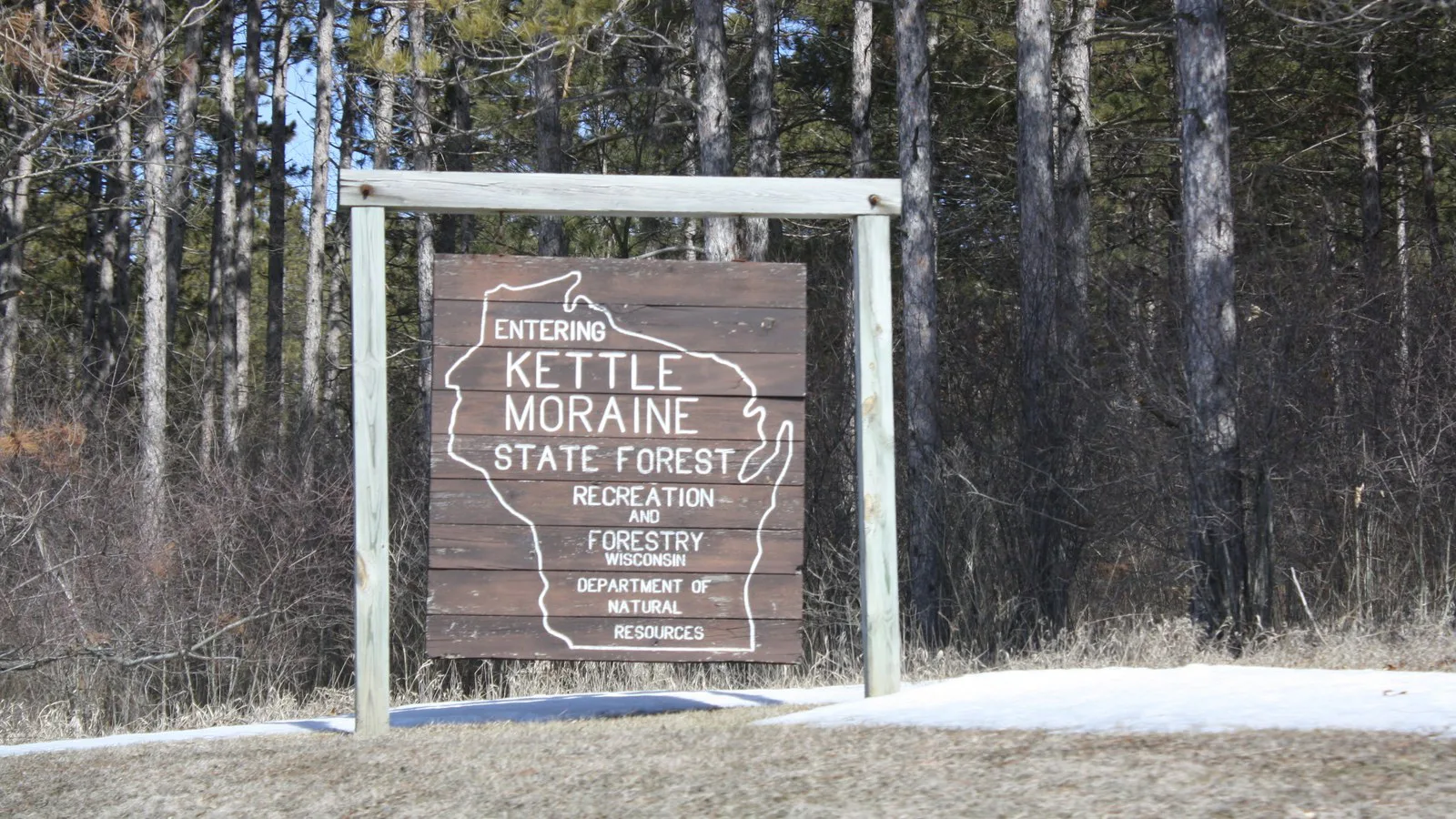 Imagem ilustrativa (não é o local do acidente): placa de madeira na entrada da unidade Sul da floresta estadual Kettle Moraine, em Wisconsin, com o contorno do mapa do estado, entre pinheiros