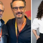 Dois homens de óculos com crachás de evento em fundo colorido, e mulher de cabelo ondulado e blusa branca em retrato