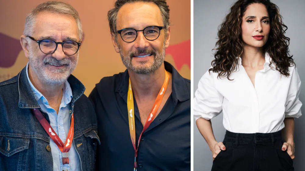 Dois homens de óculos com crachás de evento em fundo colorido, e mulher de cabelo ondulado e blusa branca em retrato
