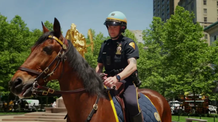 O detetive Kyle McLaughlin, de capacete, montado no cavalo Kelly numa praça arborizada de Nova York