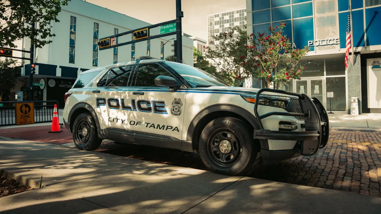 Viatura branca da polícia de Tampa estacionada numa rua do centro da cidade, ao lado de um prédio com a palavra "Police" na fachada