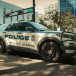 Viatura branca da polícia de Tampa estacionada numa rua do centro da cidade, ao lado de um prédio com a palavra "Police" na fachada