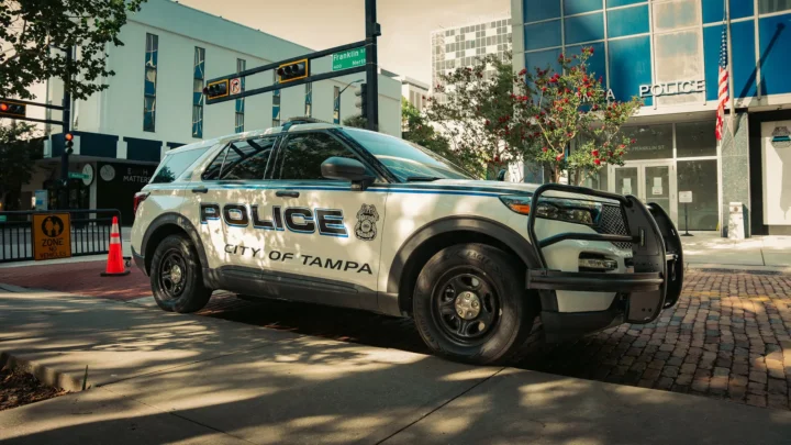 Viatura branca da polícia de Tampa estacionada numa rua do centro da cidade, ao lado de um prédio com a palavra "Police" na fachada
