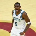 Jogador de camisa branca com detalhes azuis e verdes, número 5 e a palavra "Wolves", grita e cerra os punhos em quadra
