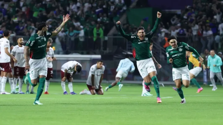 Jogadores do Palmeiras de uniforme verde comemoram com os braços erguidos, enquanto adversários de branco e vinho se abaixam no gramado após a disputa de pênaltis