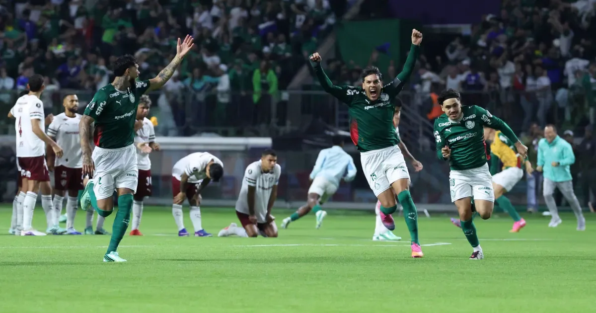 Jogadores do Palmeiras de uniforme verde comemoram com os braços erguidos, enquanto adversários de branco e vinho se abaixam no gramado após a disputa de pênaltis