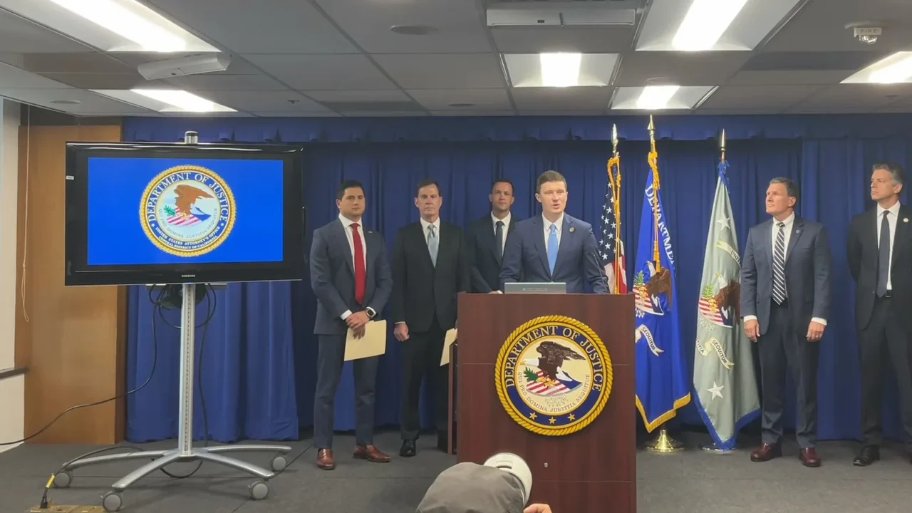 Trent McCotter, vice-procurador-geral interino, discursa no púlpito do Departamento de Justiça ao lado de procuradores federais no anúncio das acusações