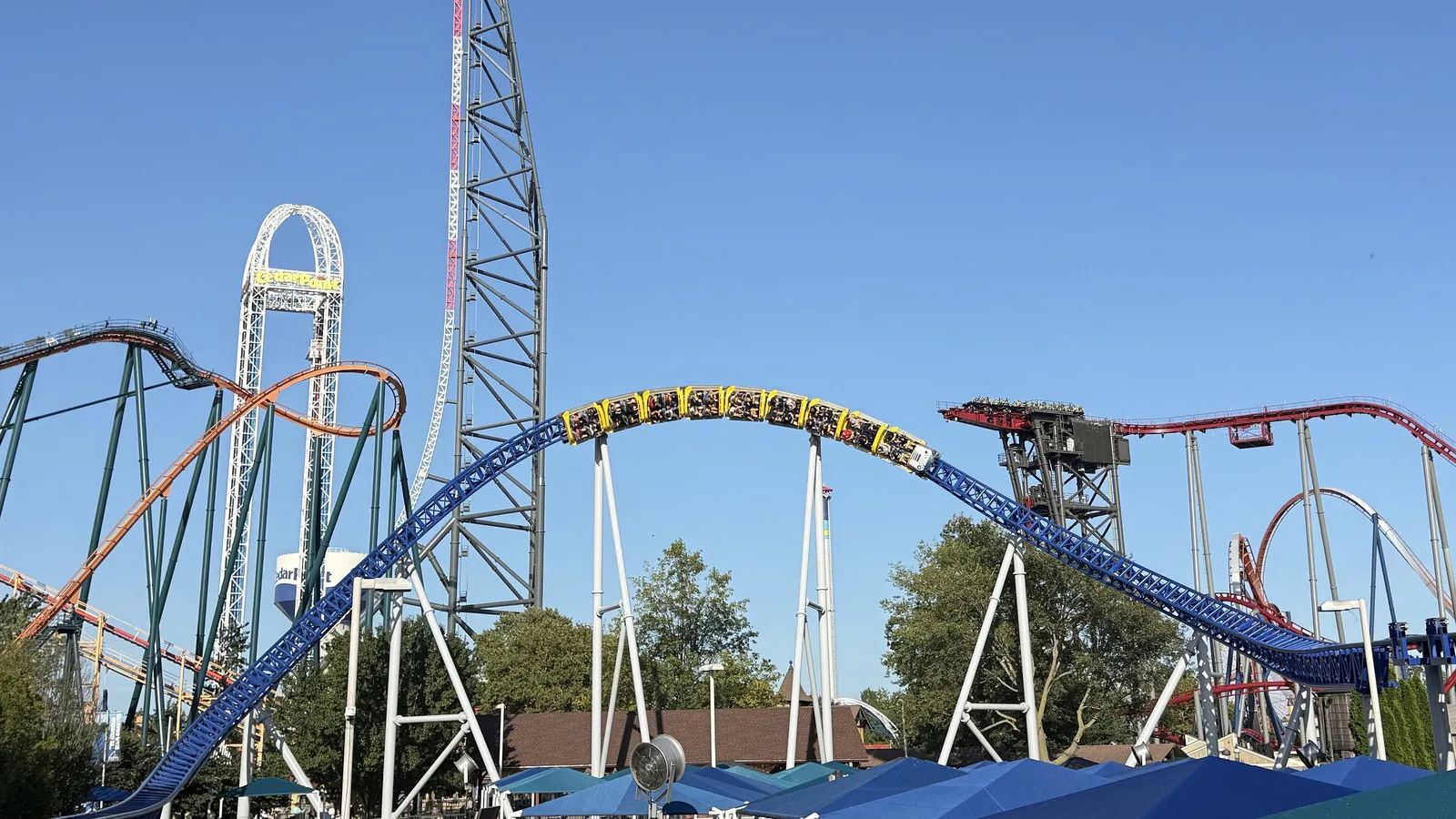 Trem da Millennium Force passa no alto de uma colina do percurso, com a torre da Top Thrill 2 ao fundo, em setembro de 2026