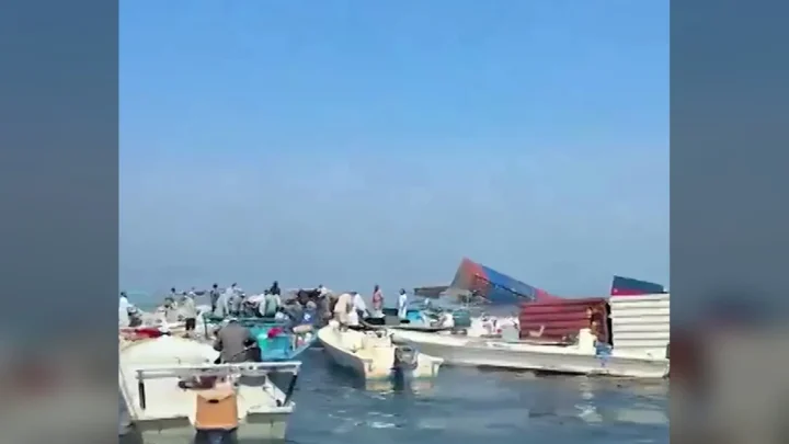 Dezenas de barcos pequenos de pescadores reunidos ao lado de contêineres boiando no Estreito de Ormuz, depois do naufrágio do GFS Pride; um homem carrega uma caixa num dos barcos