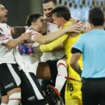 Jogadores do Estudiantes comemoram abraçados, com o goleiro de amarelo no centro do grupo, após vencer nos pênaltis