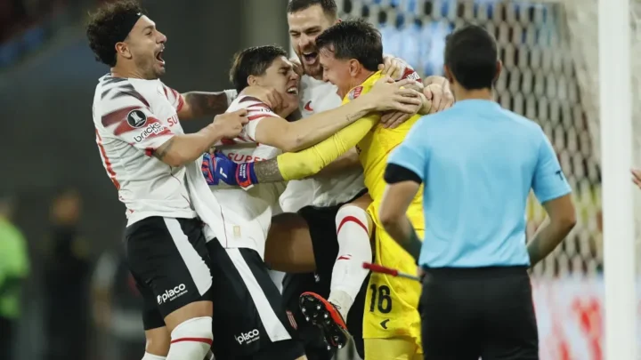 Jogadores do Estudiantes comemoram abraçados, com o goleiro de amarelo no centro do grupo, após vencer nos pênaltis