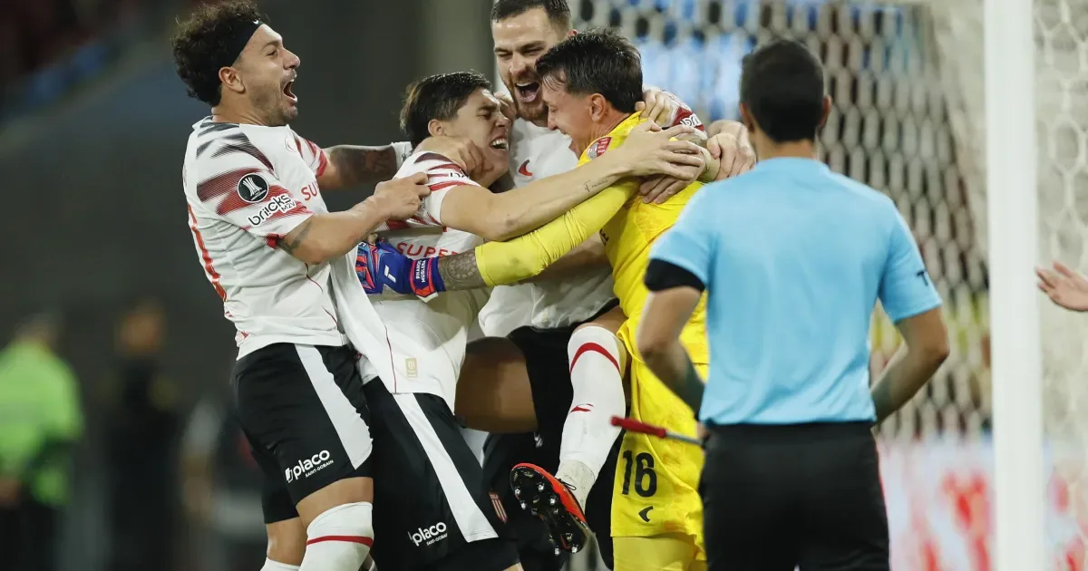 Jogadores do Estudiantes comemoram abraçados, com o goleiro de amarelo no centro do grupo, após vencer nos pênaltis