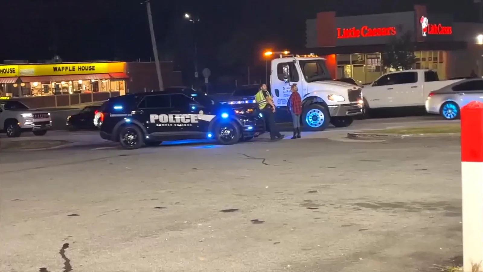 Viatura da polícia de Powder Springs com as luzes ligadas perto da entrada dos postos, à noite