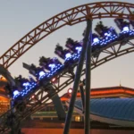 Foto de arquivo de abril de 2025, ao entardecer, de um trem da montanha-russa Stardust Racers com as luzes acesas no Epic Universe, em Orlando; a foto não mostra a fila nem o ventilador