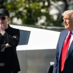 Elon Musk, de boné, óculos escuros e roupa preta, com a mão no queixo, ao lado de Donald Trump, de terno e gravata vermelha, diante de uma Cybertruck no gramado sul da Casa Branca, em março de 2025 (imagem de arquivo)