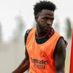 Jogador de colete laranja do Real Madrid, com o escudo do clube e o patrocínio da Emirates, observa algo fora de quadro durante treino