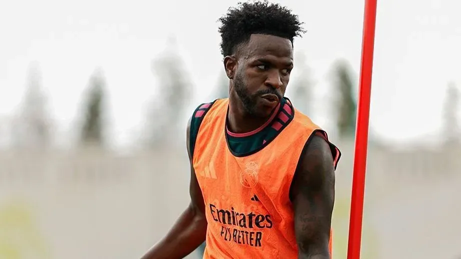 Jogador de colete laranja do Real Madrid, com o escudo do clube e o patrocínio da Emirates, observa algo fora de quadro durante treino