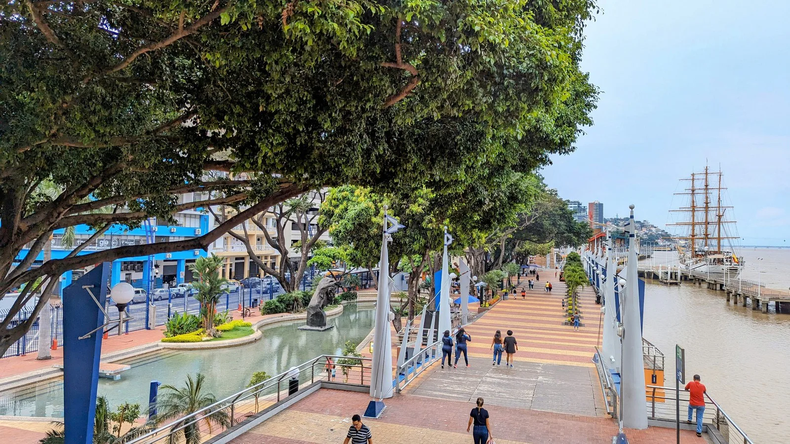 Calçadão do Malecón 2000, à beira do rio Guayas, em Guayaquil, com árvores e um veleiro ao fundo