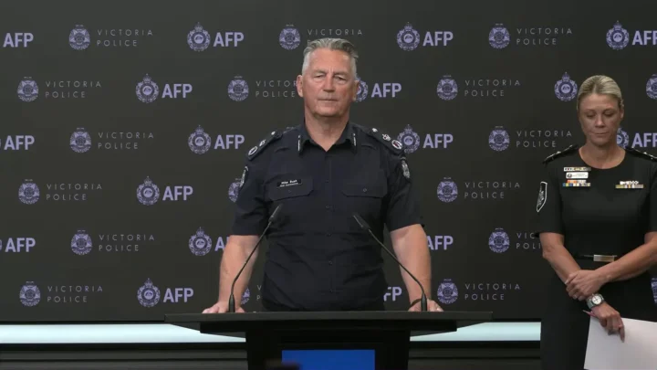 O comissário-chefe da polícia de Victoria, Mike Bush, ao púlpito, ao lado da comissária da Polícia Federal australiana, Krissy Barrett, em coletiva, em 21 de outubro de 2026
