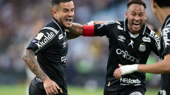 Dois jogadores do Santos com camisas pretas comemoram com muita empolgação, um deles com braçadeira vermelha, em campo de futebol
