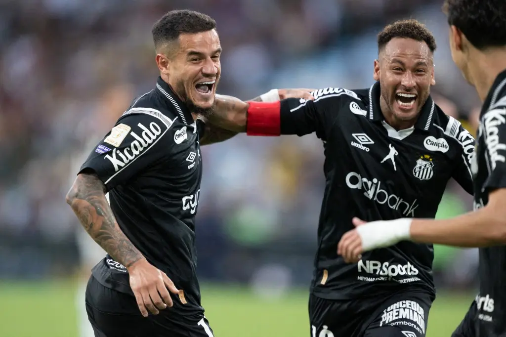 Dois jogadores do Santos com camisas pretas comemoram com muita empolgação, um deles com braçadeira vermelha, em campo de futebol