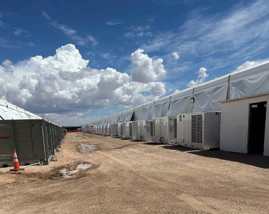 Fileira de tendas brancas e aparelhos de ar-condicionado do Camp East Montana, centro de detenção do ICE em El Paso, no Texas, em chão de terra sob céu azul (foto do GAO, sem pessoas)