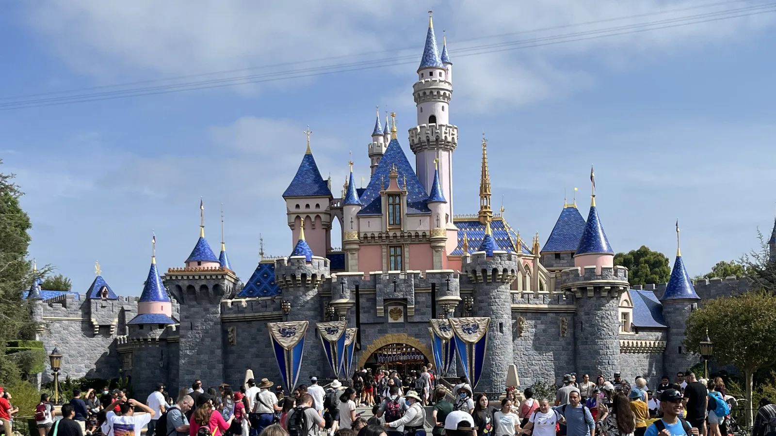 Castelo da Bela Adormecida, com torres azuis e rosa, e visitantes na praça em frente, na Disneyland, em Anaheim, em dia de sol (foto de 2022)