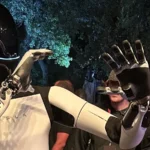 Robô humanoide Optimus, da Tesla, com capacete preto e corpo branco, acena com as mãos no meio do público num evento da empresa nos estúdios da Warner Bros., na Califórnia, em outubro de 2024 (imagem de arquivo)