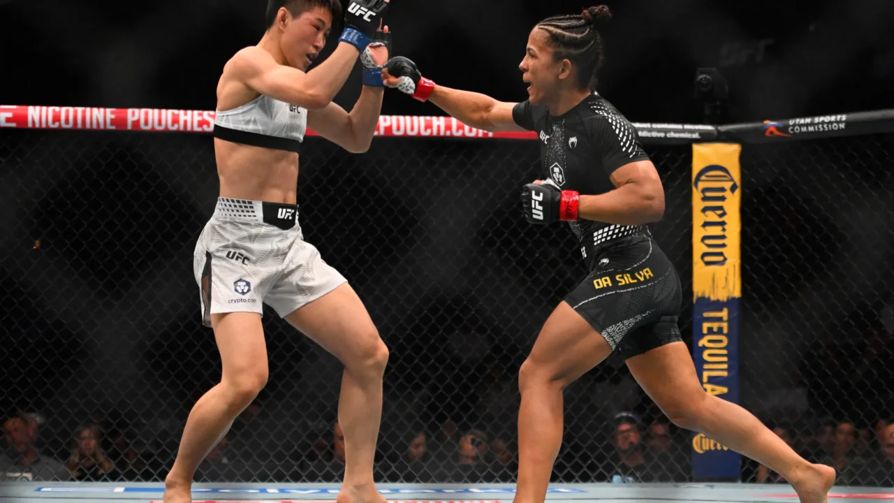 Duas lutadoras de MMA em confronto dentro do octógono durante evento da UFC, com uma delas em uniforme branco e a outra em preto com detalhes em vermelho e ouro