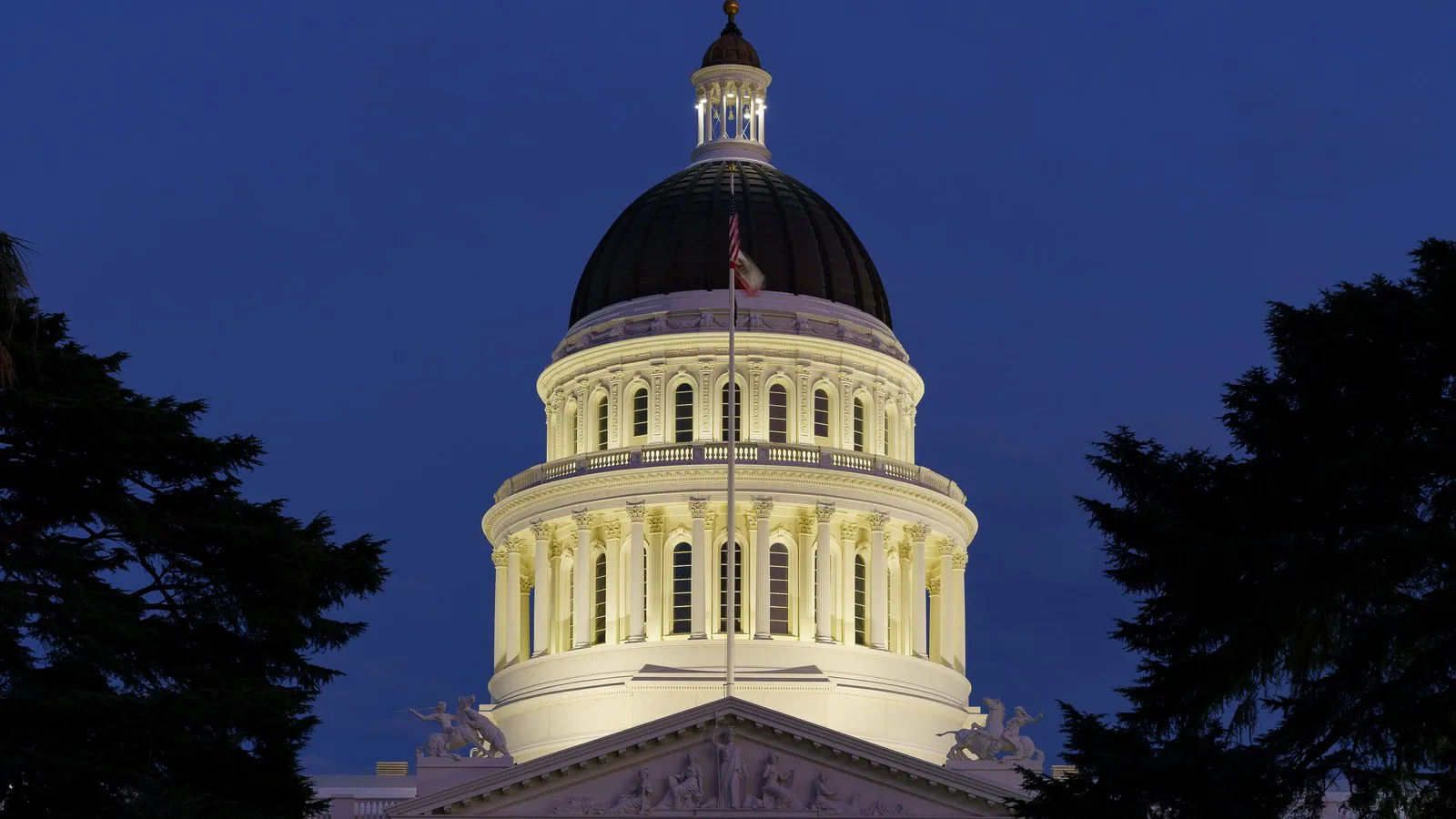 Cúpula iluminada do Capitólio da Califórnia, sede do governo estadual em Sacramento, ao anoitecer, entre árvores escuras (imagem de arquivo de 2021)