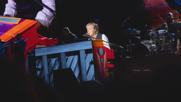 Paul McCartney toca teclado em apresentação ao vivo com banda ao fundo, em show com iluminação colorida