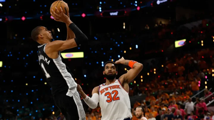 Jogador de camisa preta do San Antonio Spurs arremessa sob marcação do defensor do New York Knicks, o número 32, em jogo de basquete na NBA