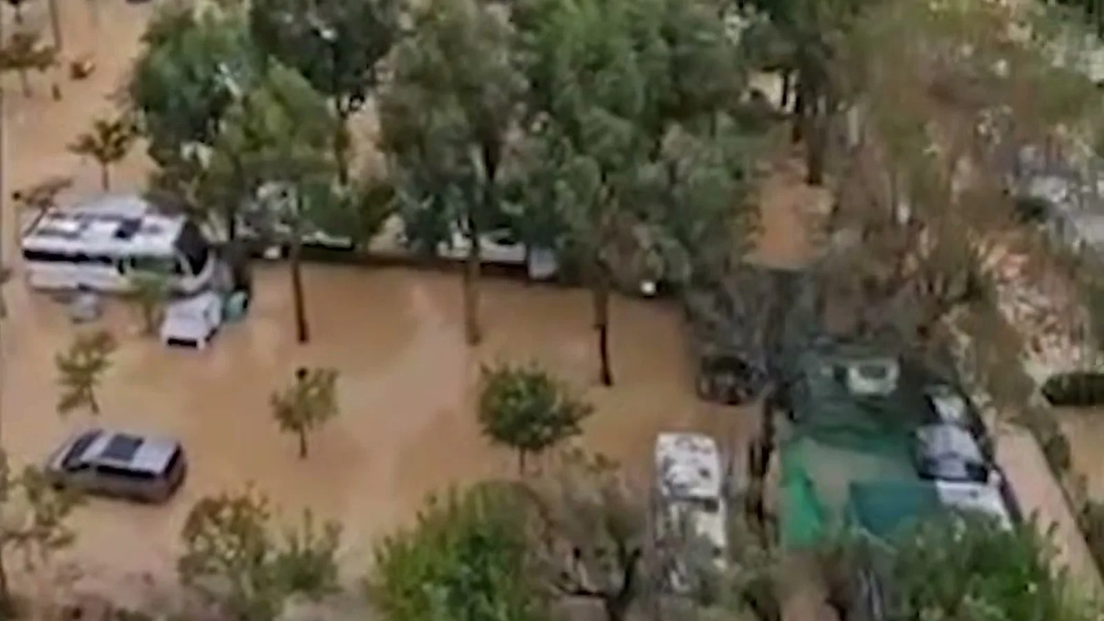 Vista aérea de um camping tomado pela água barrenta, com trailers e carros parados entre as árvores, no entorno de Oliva