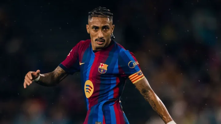 Jogador de camisa listrada em azul e grená, com braçadeira do Barcelona, olha em direção ao campo durante uma partida noturna