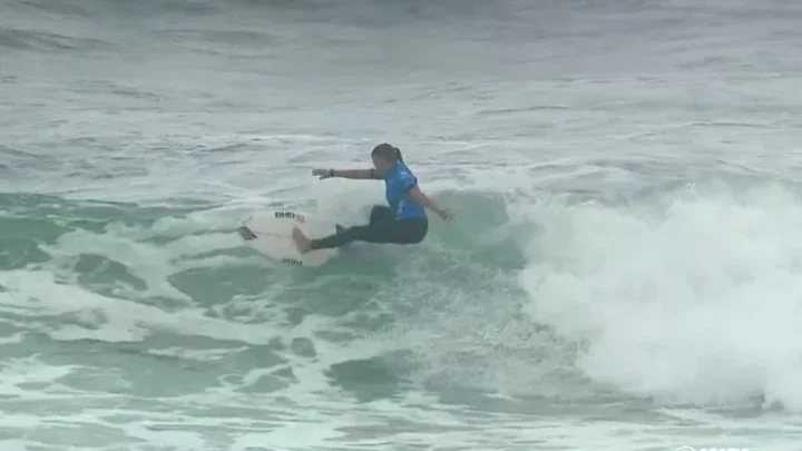 Surfista em traje azul manobra sobre onda durante competição de surfe