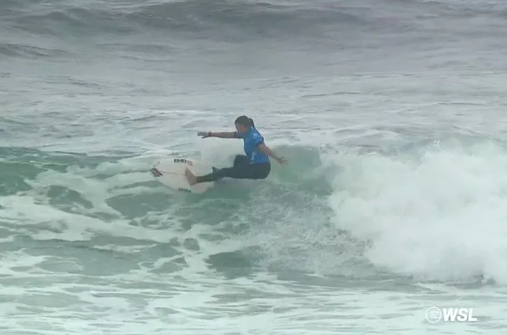 Surfista em traje azul manobra sobre onda durante competição de surfe