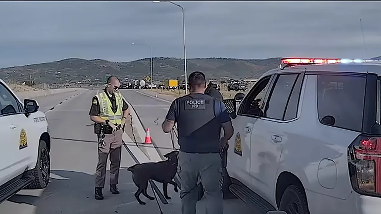 O policial Wayne Henderson, de colete, ao lado do cão Bruno, um labrador chocolate, entre viaturas da Patrulha Rodoviária de Utah no viaduto interditado
