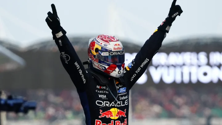 Piloto da Red Bull comemora com os braços levantados ao vencer corrida de Fórmula 1, usando capacete com patrocinadores e macacão da equipe com logos de Red Bull e Oracle