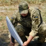 Soldado das Forças de Apoio da Ucrânia, de boné e farda camuflada, monta uma antena da Starlink no chão, em julho de 2022 (imagem de arquivo)