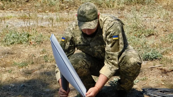 Soldado das Forças de Apoio da Ucrânia, de boné e farda camuflada, monta uma antena da Starlink no chão, em julho de 2022 (imagem de arquivo)