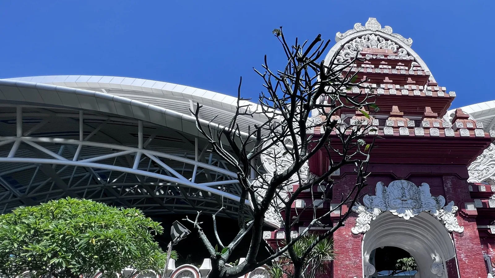 Portal de arquitetura balinesa, de tijolos vermelhos e pedra branca entalhada, diante da cobertura metálica do terminal internacional do aeroporto de Bali (foto de arquivo)