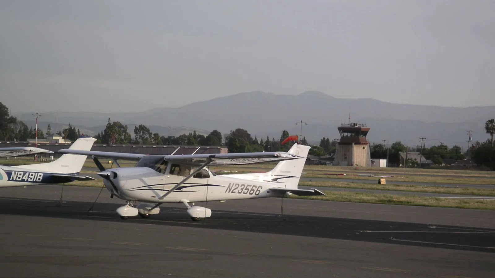 Pequeno avião na pista do aeroporto Reid-Hillview, com a torre de controle e as montanhas ao fundo