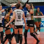 Jogadoras de vôlei com uniformes pretos e brancos comemoram um ponto em quadra, com a camisa 10 de Michelle de costas