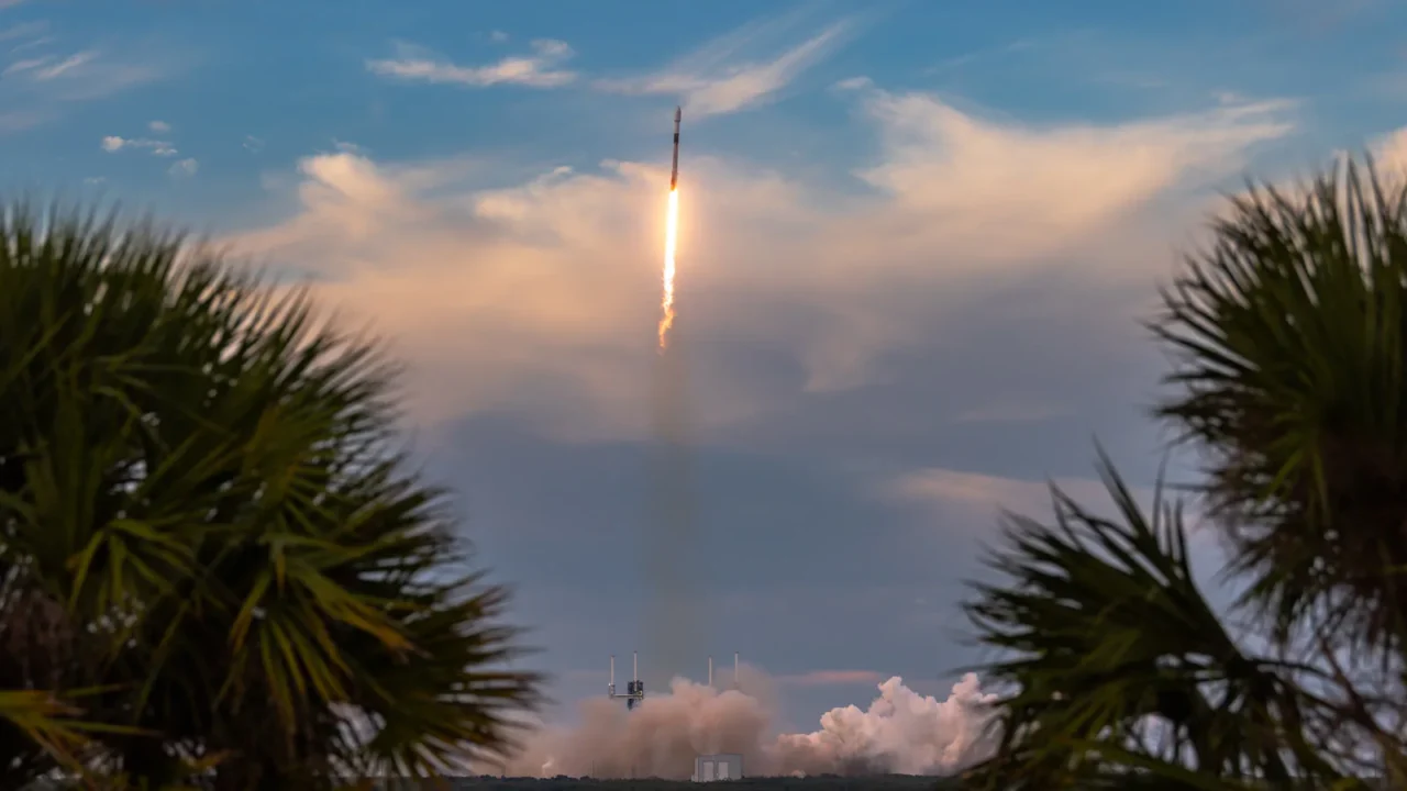 Foguete Falcon 9 sobe sobre a água deixando um rastro de fumaça, emoldurado por palmeiras, no Cabo Canaveral, na Flórida
