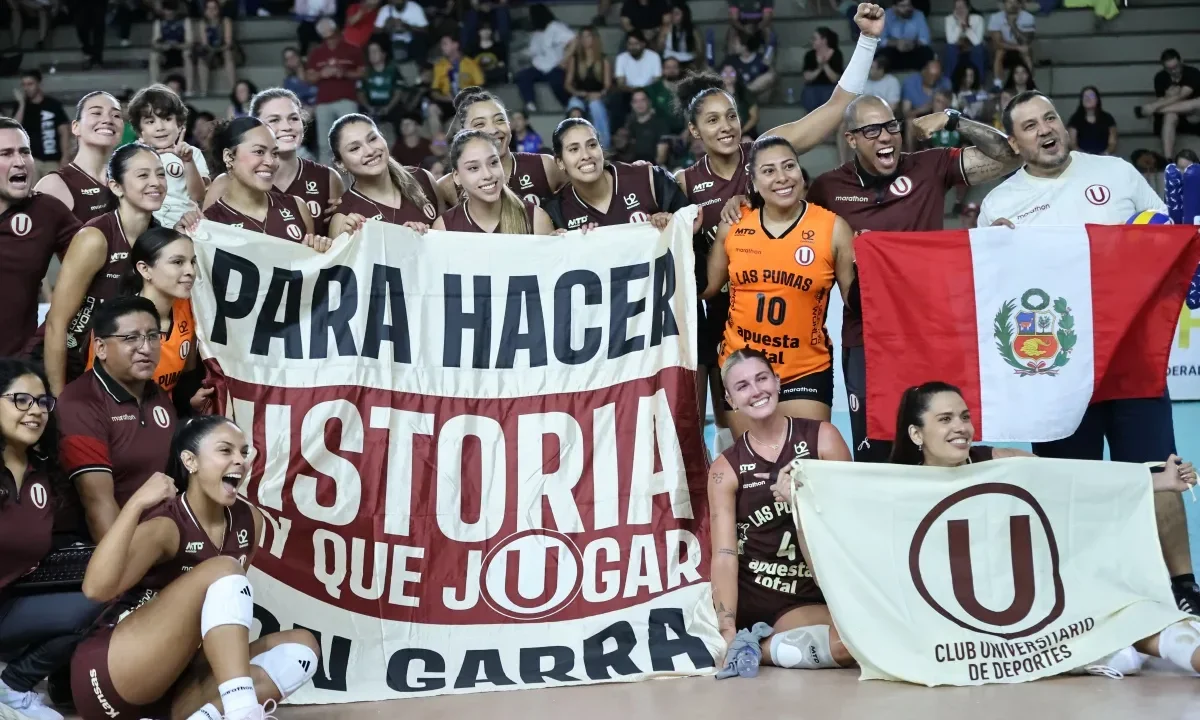 Equipe de voleibol feminino em uniforme vinho comemora vitória segurando bandeiras e faixas com mensagens de apoio em quadra coberta repleta de torcedores