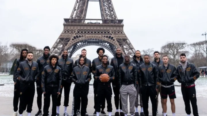 Grupo de pessoas em uniformes esportivos pretos posam segurando uma bola de basquete diante da Torre Eiffel