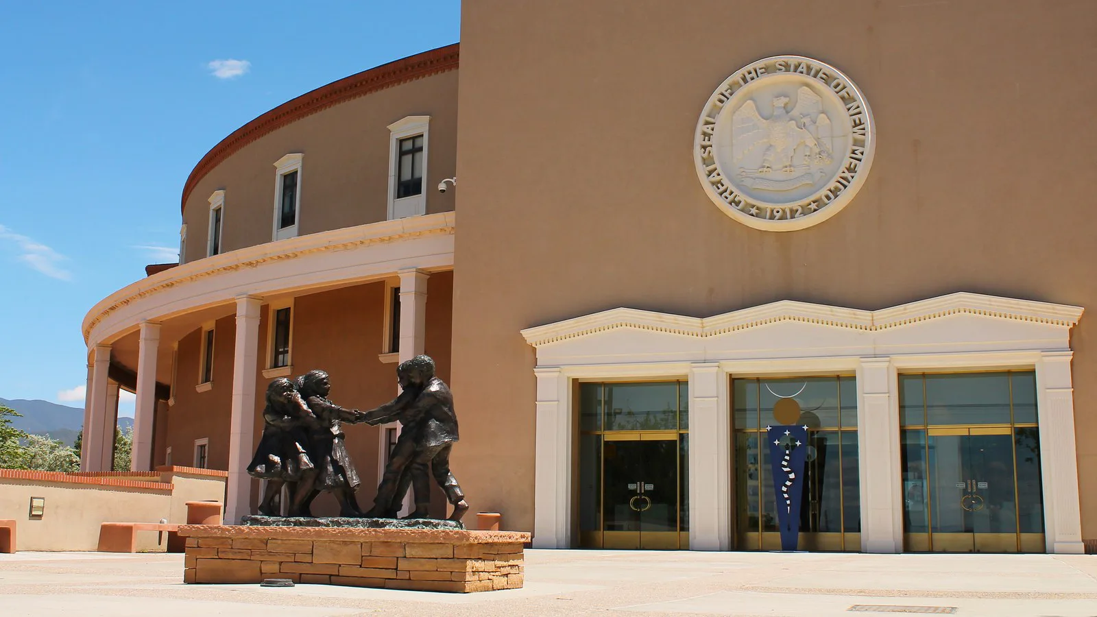 Fachada do Capitólio do Novo México, em Santa Fe, com o selo do estado sobre a entrada e uma escultura de bronze de crianças à frente