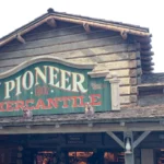 Fachada de madeira da loja Pioneer Mercantile, com placa verde e letras vermelhas, na Frontierland da Disneyland, em Anaheim, na Califórnia, em dia seco (foto de 2019)